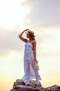 Woman in a flowing plaid-print dress paired with a black hat, resort-casual styling — placeholder image