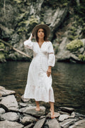 Woman in a flowing satin-look dress on a rocky shoreline — placeholder image