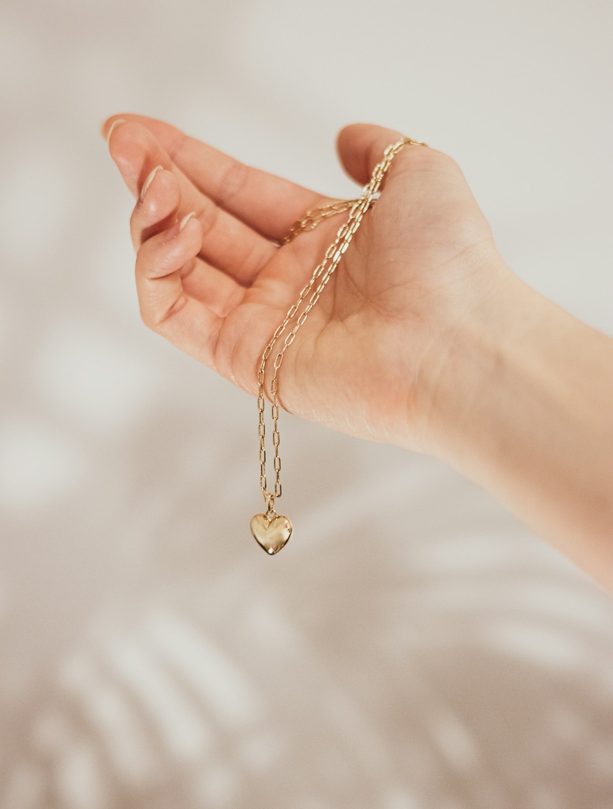 Delicate gold heart charm on a fine chain, held in hand — placeholder image